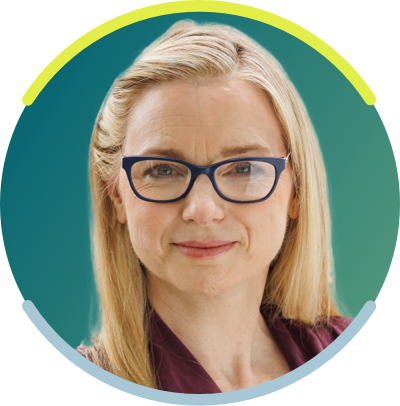A white woman with long blonde hair and dark glasses is seen from the neck up. She faces the camera with a neutral smile