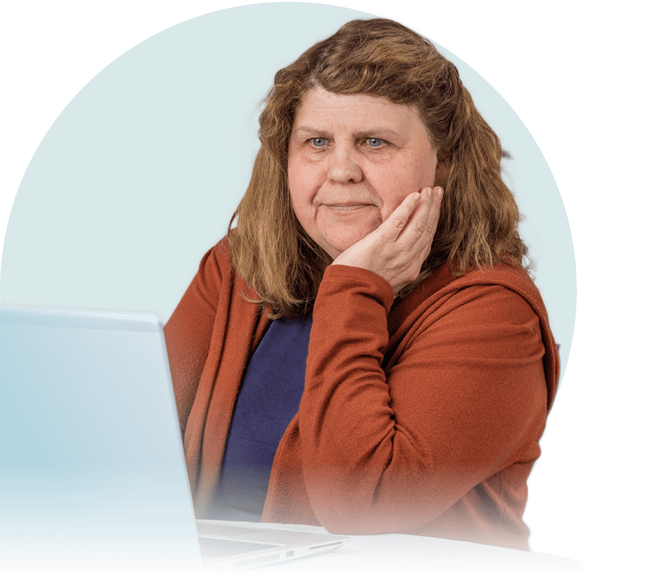 A white woman with brown hair is seen from the waist up. She is seated and looking at a laptop
