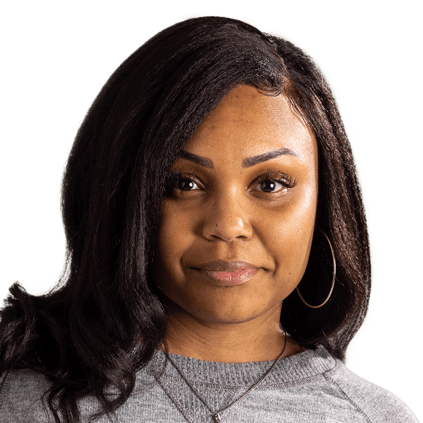 An African-American woman with long brown hair is seen from the neck up. She faces the camera with a neutral smile