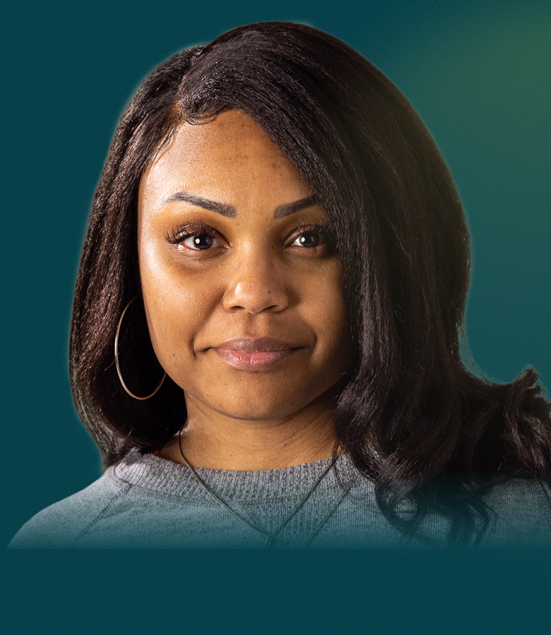 An African-American woman with long brown hair is seen from the neck up. She faces the camera with a neutral smile