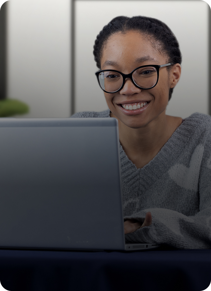 A young African-American woman with braided hair and dark-framed glasses is seen from the neck up, smiling