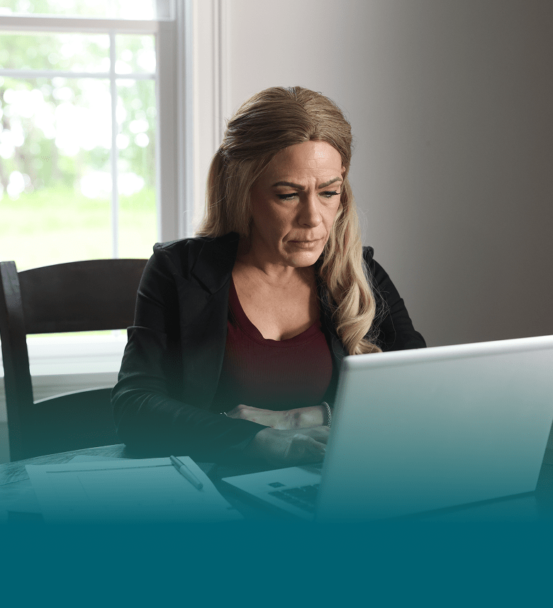 A white woman with blonde hair looks down at her laptop computer. She is seen from the chest up