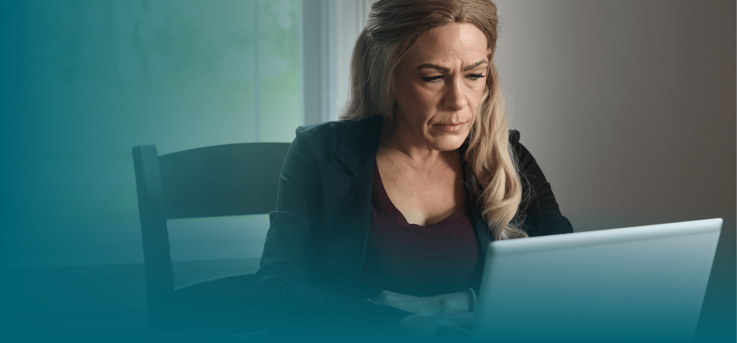 A white woman with blonde hair looks down at her laptop computer. She is seen from the chest up