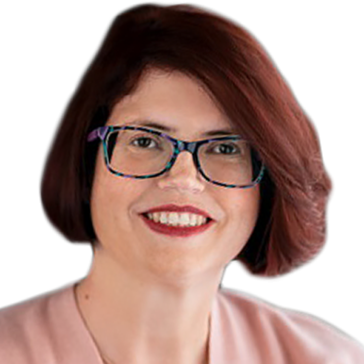 A white woman with short brown hair and patterned glasses is seen from the neck up. She faces the camera with a smile that reveals her teeth