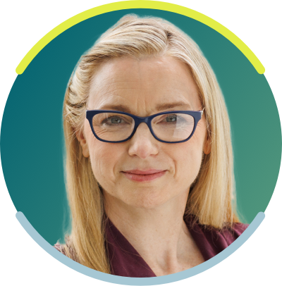 A white woman with long blonde hair and dark glasses is seen from the neck up. She faces the camera with a neutral smile