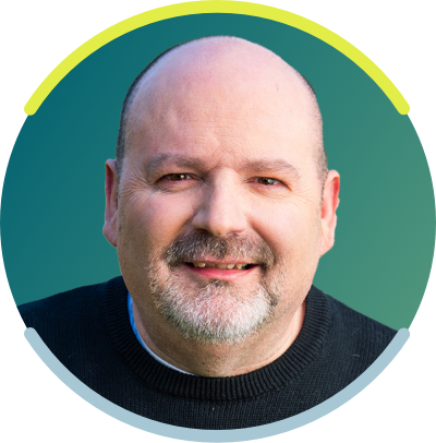 A bald white man with a gray goatee is seen from the neck up. He is smiling