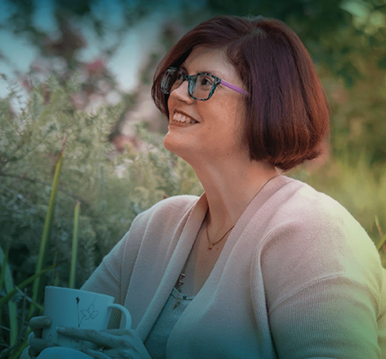 A white woman with short brown hair and glasses. She is seen from the shoulders up, she is smiling and looking towards the top left corner of the photo.