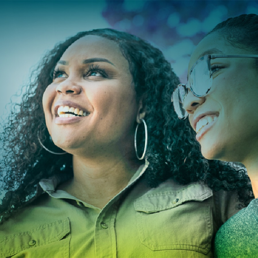 An African-American mother and daughter are seen from the neck up, smiling, and looking off camera to the left
