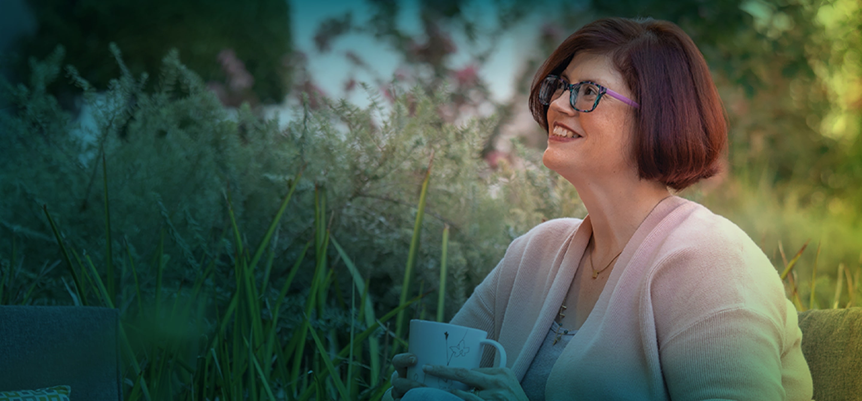 A white woman with short brown hair and glasses. She is seen from the shoulders up, she is smiling and looking towards the top left corner of the photo. 