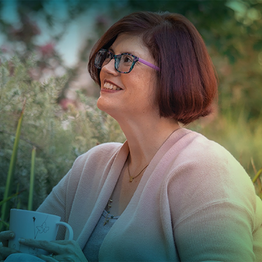 A white woman with short brown hair and glasses. She is seen from the shoulders up, she is smiling and looking towards the top left corner of the photo. 