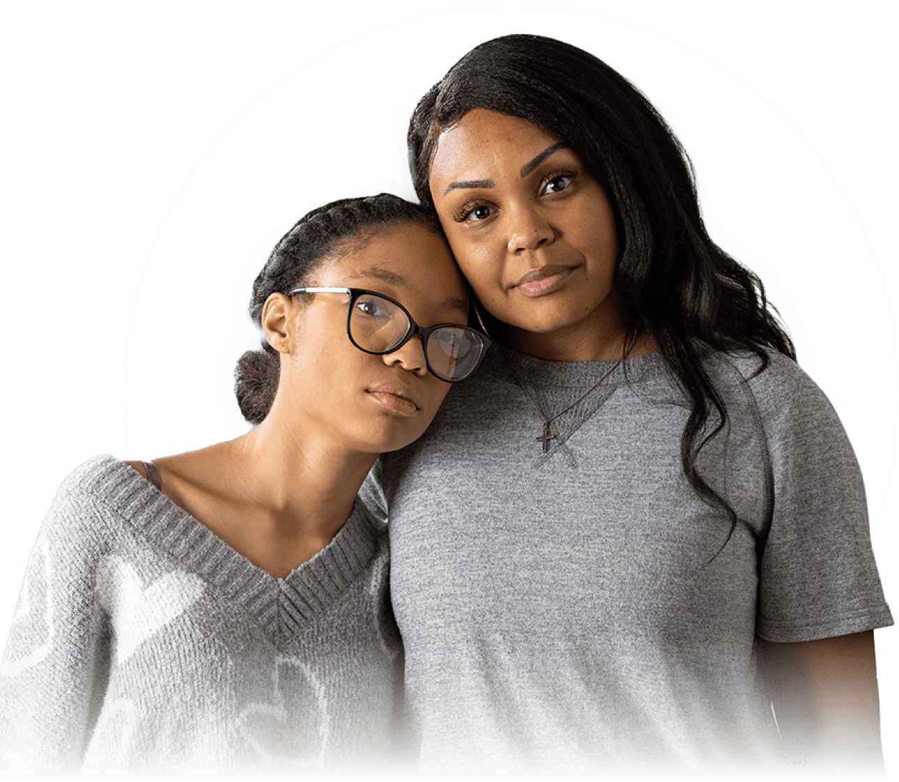 A young African-American girl in dark glasses leans on an older African-American woman with long brown hair. The pair are seen from the waist up and they both have neutral expressions