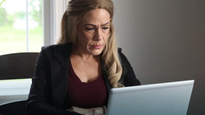 A white woman with blonde hair looks down at her laptop computer. She is seen from the neck up