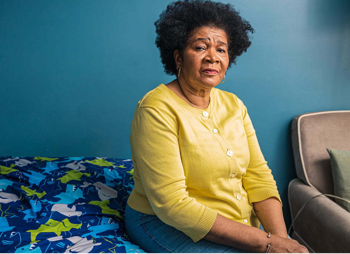 An African-American woman with short, curly black hair is seen from the chest up. She is wearing a yellow cardigan and sitting facing the camera with a neutral expression.