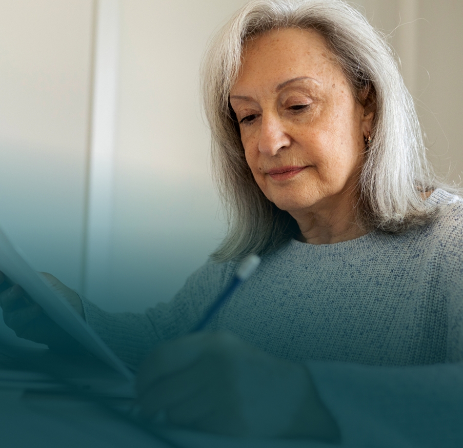 Actor portrayal of a senior woman sitting and looking down at a paper.