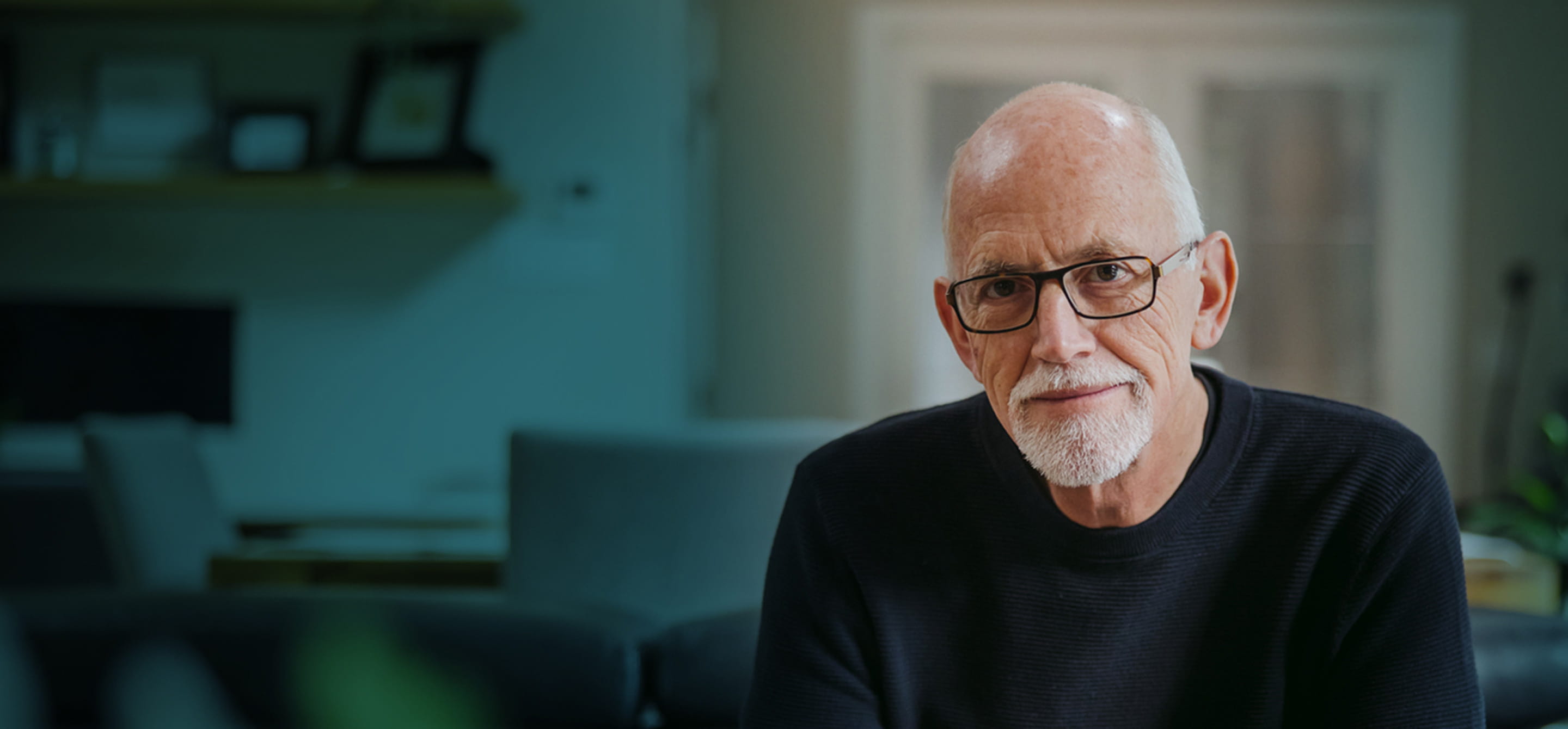 An older white man with white hair, a goatee, and black-rimmed glasses, seen from the chest up.
