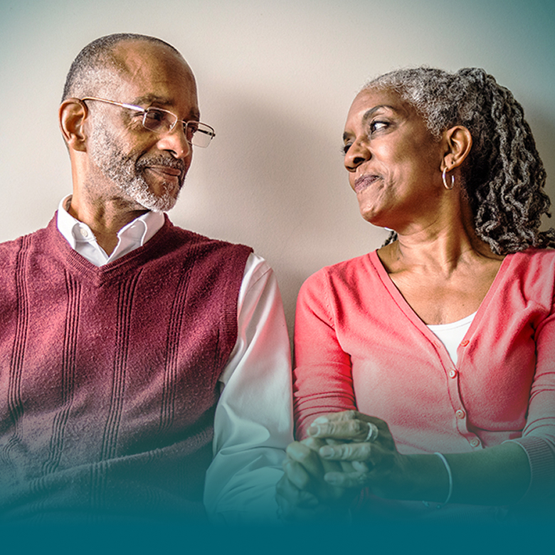 An African American man and an African American woman are seated next to each other, holding hands, and looking at each other supportively.
