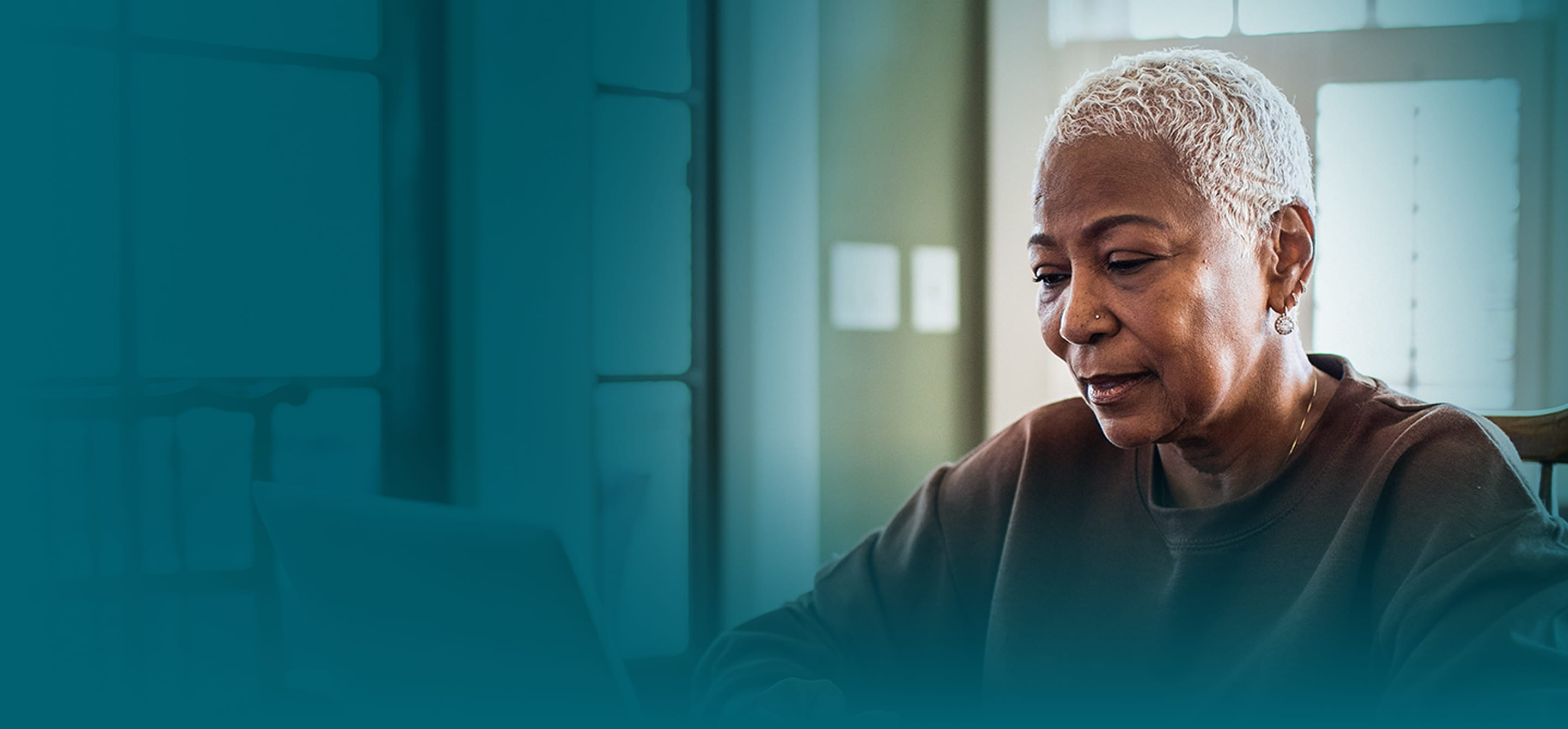 An African-American woman with short blonde hair is wearing a brown sweatshirt. She is typing on a keyboard, looking at a laptop screen with a neutral expression. ﻿