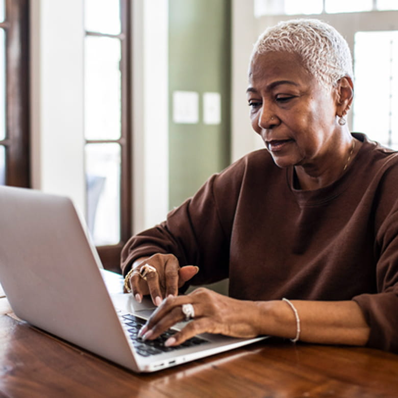 An African-American woman with short blonde hair is wearing a brown sweatshirt. She is typing on a keyboard, looking at a laptop screen with a neutral expression. ﻿