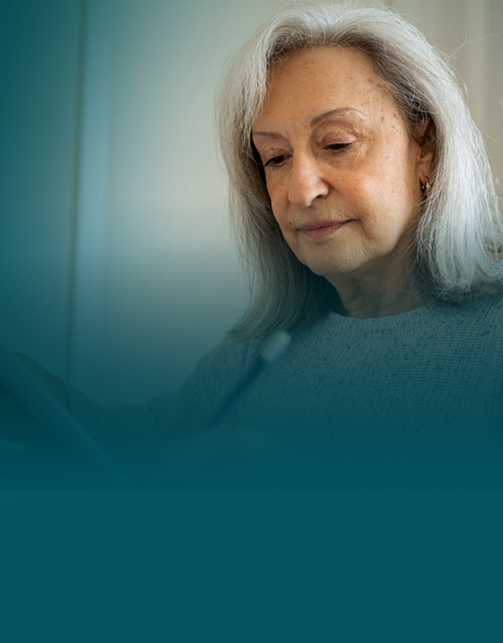 Actor portrayal of a senior woman sitting and looking down at a paper.