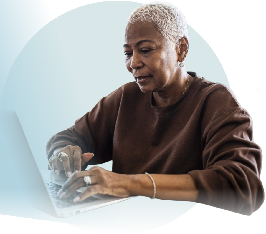 An African-American woman with short blonde hair is wearing a brown sweatshirt. She is typing on a keyboard, looking at a laptop screen with a neutral expression.
