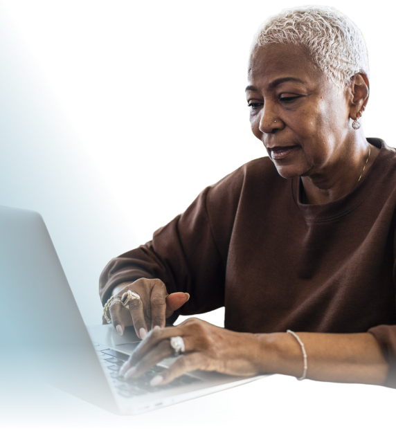 An African-American woman with short blonde hair is wearing a brown sweatshirt. She is typing on a keyboard, looking at a laptop screen with a neutral expression.