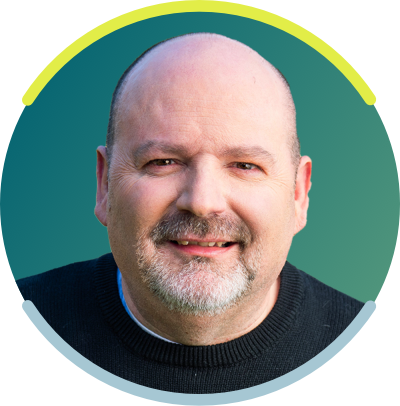 A bald white man with a gray goatee is seen from the neck up. He is smiling