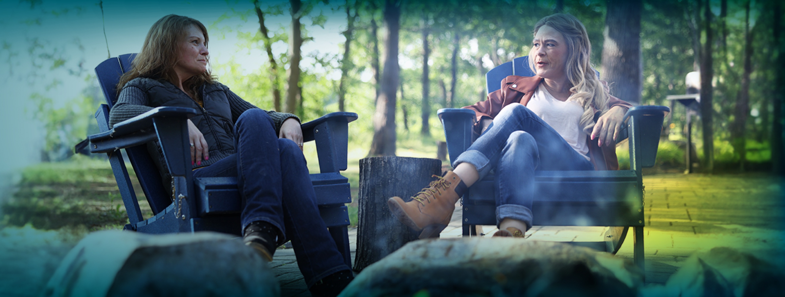 Two white women sitting in outdoor recliner chairs. They are turned towards each other in mid-conversation. 
