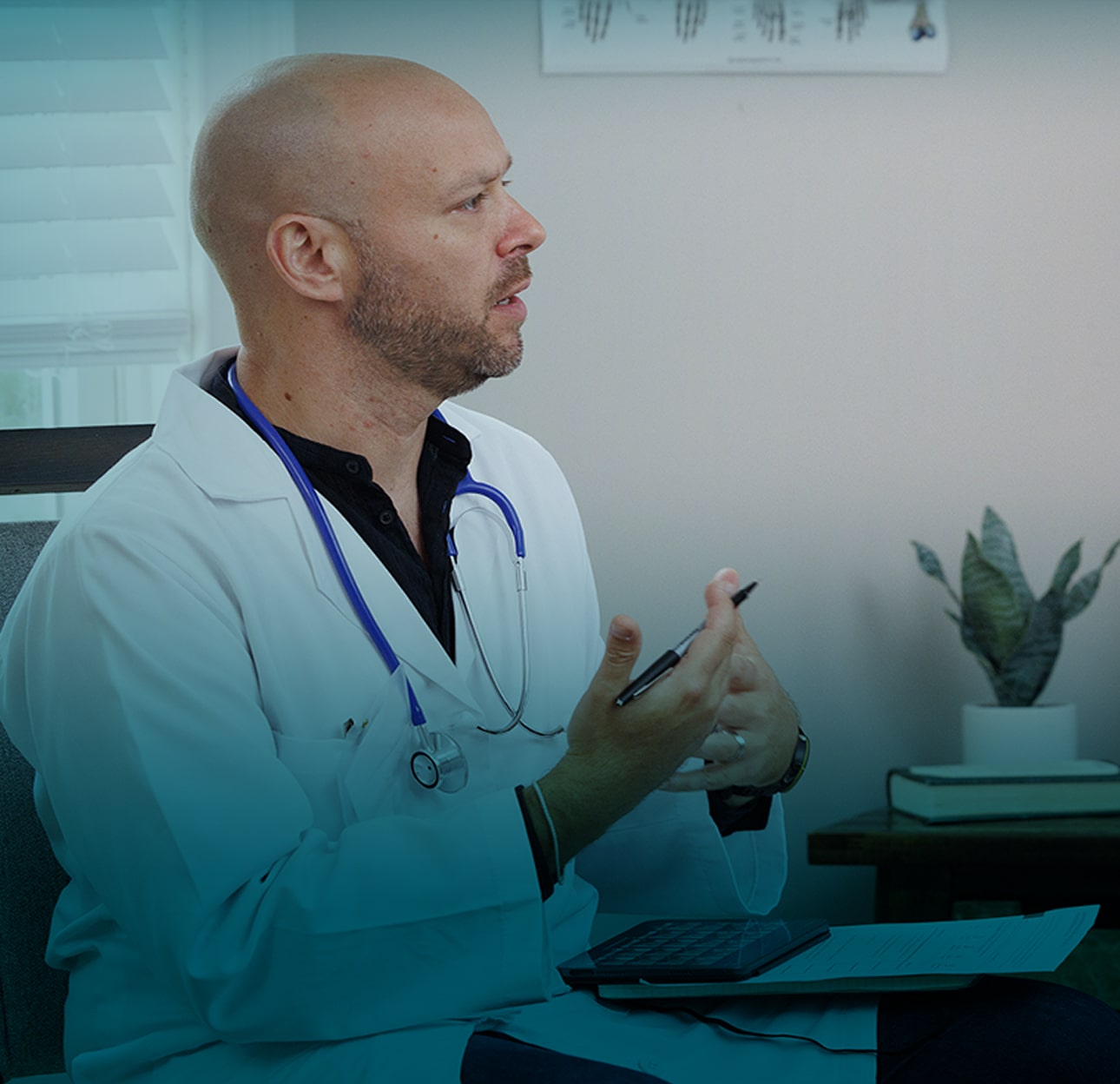 The doctor, a bald white man with a beard in a white lab coat and stethoscope, sits in his office facing a patient, a white woman with long blonde hair 